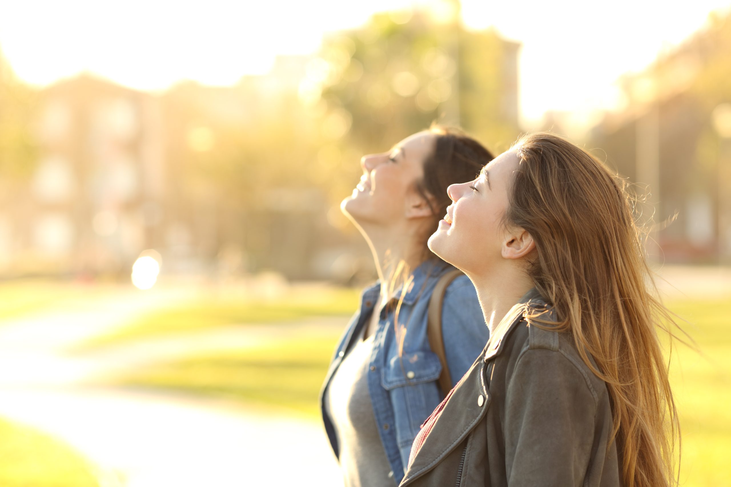 Side View Portrait of Two Happy Girls Breathing Fresh Air Together in a Park at Sunset